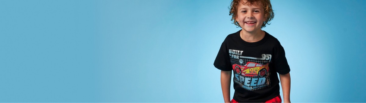 Boy with curly hair wearing a Lightning McQueen blueprint-style t-shirt with black background and text Built For Speed: Zero to 60 in 4 Seconds.