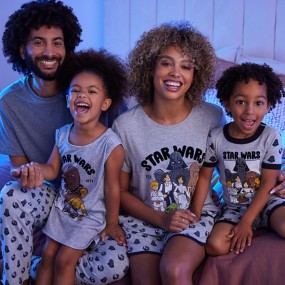 Family wearing matching gray Star Wars pajamas sitting on a bed smiling and hugging.
