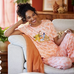 Woman with brown curly hair in a ponytail wearing peach-colored Lion King pajamas on a couch.