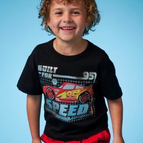 Boy with curly hair wearing a Lightning McQueen blueprint-style t-shirt with black background and text Built For Speed: Zero to 60 in 4 Seconds.