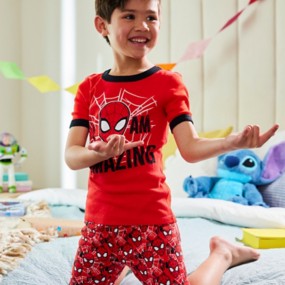 Boy with brown hair posing like Spider-Man wearing red Spider-Man Pajamas with “I am amazing” text on the top and a web pattern on the bottoms featuring Spider-Man’s face.