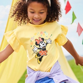 Little girl wearing a yellow Minnie Mouse t-shirt with ruffled sleeves playing outside.