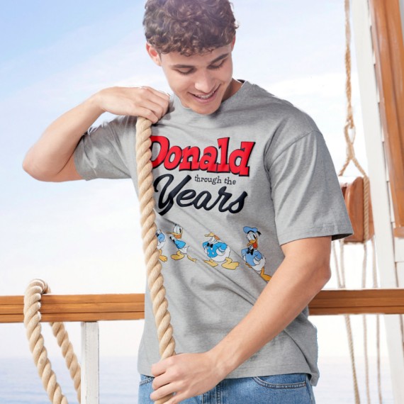 Young man on a boat holding a rope & wearing a gray t-shirt with a progression of all the different Donald Duck designs and text that reads “Donald Through The Years”.