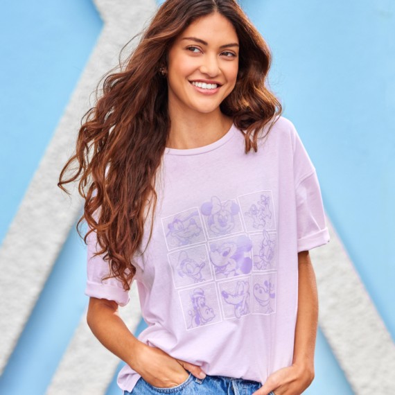 Young woman standing in front of a blue wall wearing a purple Mickey and Friends tee with a grid of characters outlined in purple.