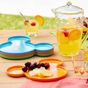 Colorful Mickey-shaped outdoor plates with clear drink pitcher and glasses, featuring subtle Mickey detail, displayed on a picnic table outside.