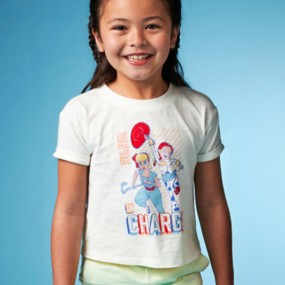Little girl with dark brown hair wearing a white graphic t-shirt for girls with Bo Peep and Jessie from Toy Story. Features We're in Charge text.