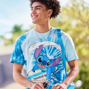 Young man wearing a light and dark blue tie dye short sleeve t-shirt featuring a center design of Stitch riding a surfboard on a wave.
