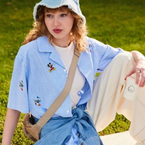 Young woman with blonde curly hair wearing a Disney short-sleeve button-down shirt blue seersucker with embroidered Mickey and friends characters.