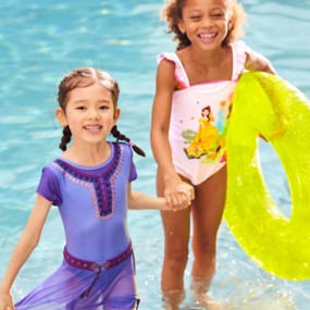 Two little girls in pool: one in Disney Wish Asha swimsuit, other holding green floatie in pink Disney Princess one piece.