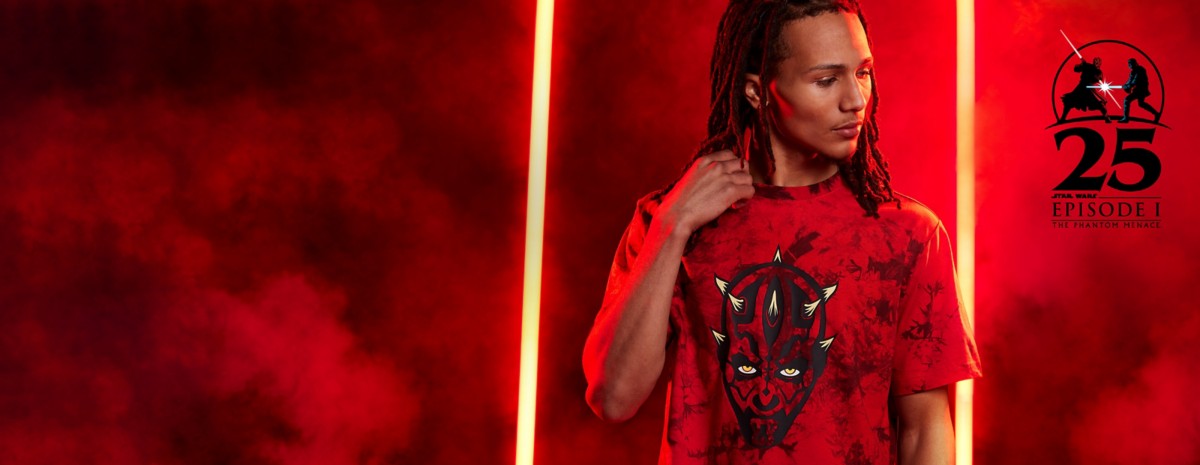Man with dreads in red Darth Maul tie dye shirt. Red backdrop with Darth Maul fight scene and Phantom Menace 25th anniversary icon.