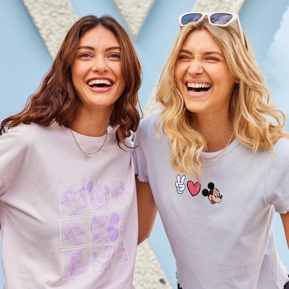 A brunette woman wearing a purple t-shirt featuring Mickey and Friends characters next to a blonde woman wearing a gray lettuce-edge Disney shirt with a Mickey Mouse embroidered design.