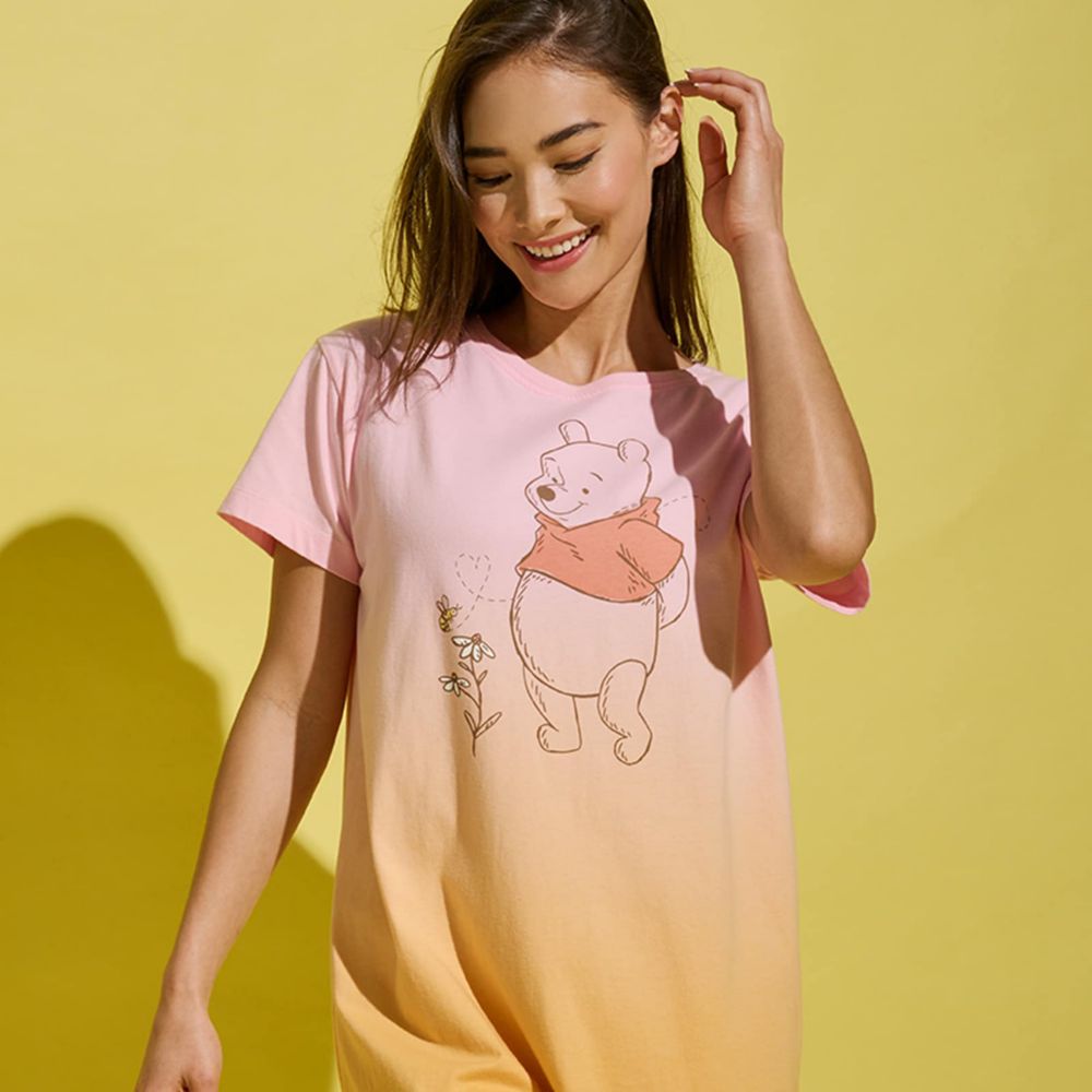 Woman with brown curly hair in a ponytail wearing peach-colored Lion King pajamas on a couch.