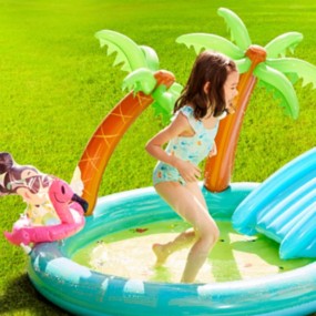 Brunette young girl in a bathing suit playing in an inflatable pool featuring Mickey and Minnie Mouse, a slide, and inflatable palm trees.