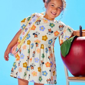 Young girl with brown hair wearing an Encanto-themed vibrant coral peasant dress for girls with colorful florals and butterflies in blue, pink, yellow, and green.